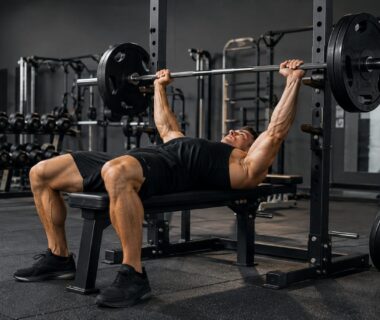 Athletic man performing heavy barbell presses in a realistic, well-equipped strength training gym