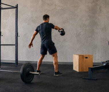 Strength athlete performing kettlebell intervals beside barbells in a bright, realistic training gym