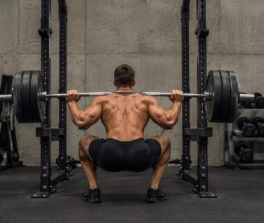 Natural bodybuilder performing a controlled barbell squat in a realistic, well-equipped gym
