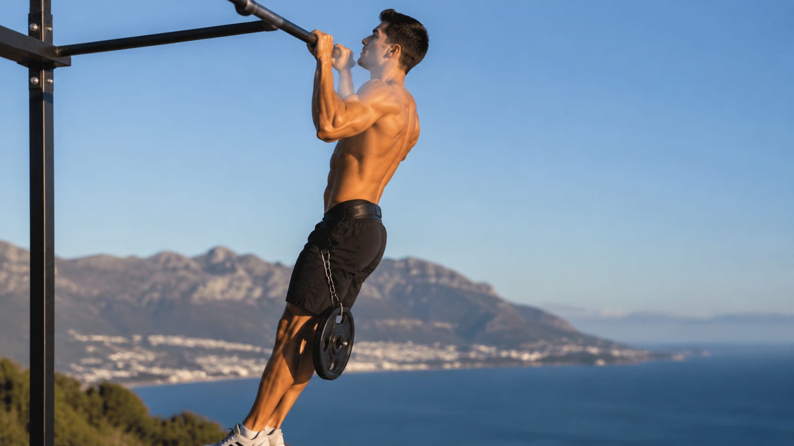 Side-profile athlete demonstrating strict weighted pull-up form with shoulders braced and legs still