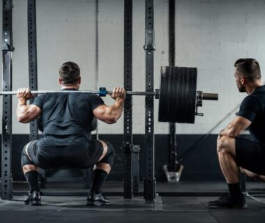 Advanced strength athlete squatting with a barbell and velocity sensor in a realistic gym