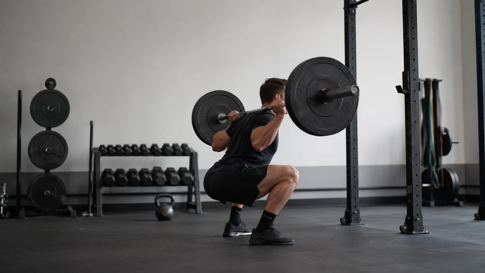 Strength athlete performing controlled barbell squats, surrounded by plates and functional gym equipment