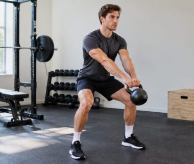 Profiled athlete performing a powerful kettlebell swing in a bright uncluttered home gym